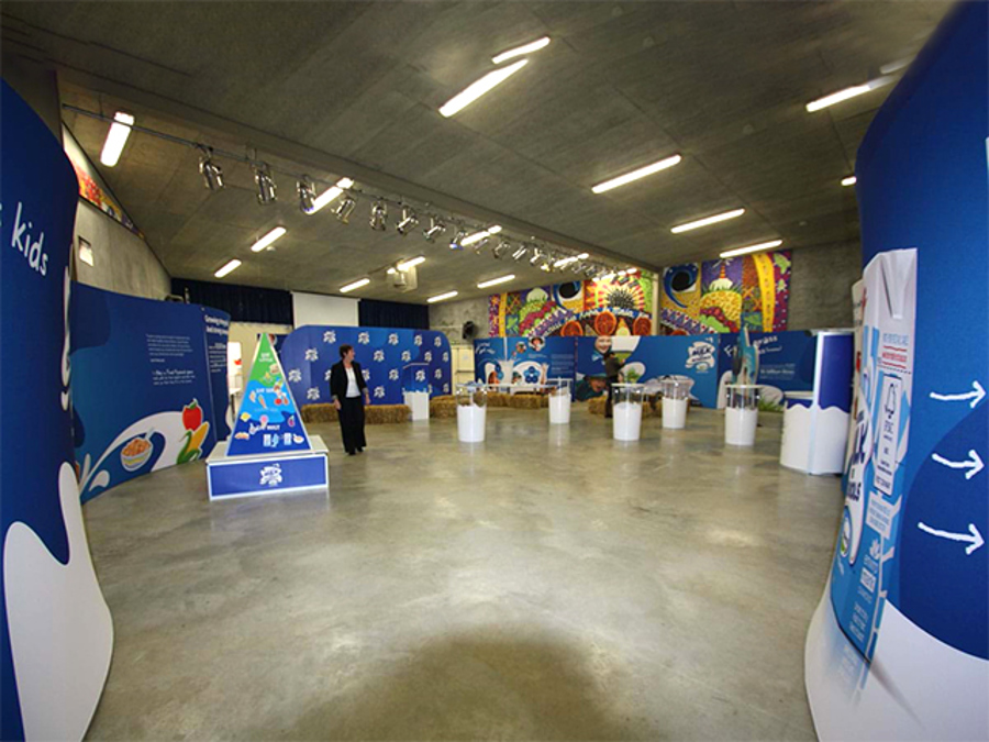 Launch set-up in a large hall with curved blue printed display walls, a food pyramid display on a low branded base, hay bales and white cylinder plinths along the walls