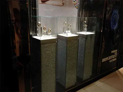 Three sparkling plinths with lit tops holding gold and silver watches under clear cases
