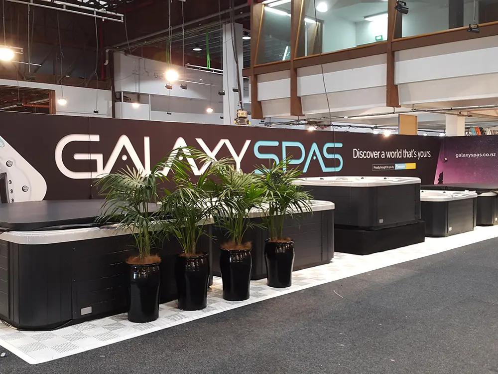 Galaxy Spas wall behind a row of spa pools on white tiles with potted palms