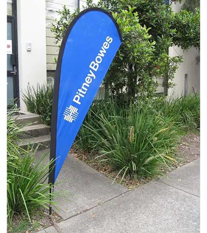 Blue Pitney Bowes teardrop flag with white vertical lettering beside a garden path