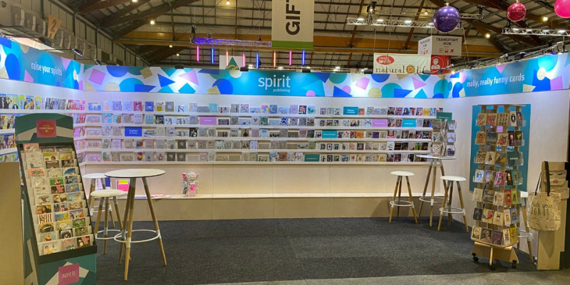 Spirit Publishing 6x3m gift fair stand with greeting cards on birch plywood shelving under a lit printed header