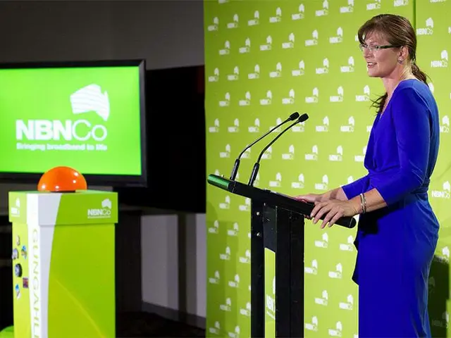 NBN Co lectern and repeated-logo wall with a large orange button on a branded plinth