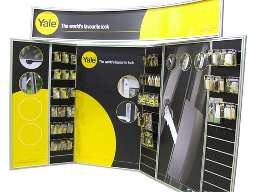 Yale product display wall with slat wall panels holding packaged locks, printed graphic panels and a curved header sign