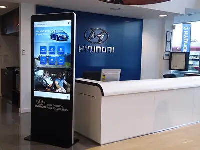 Hyundai information kiosk showing driver reviews beside a reception desk and blue feature wall