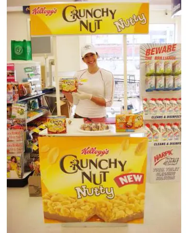 Promoter offering Kellogg's Crunchy Nut tastes at a yellow-headed table in a supermarket aisle