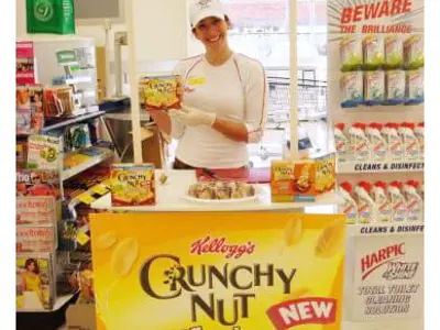 Promoter offering Kellogg's Crunchy Nut tastes at a yellow-headed table in a supermarket aisle