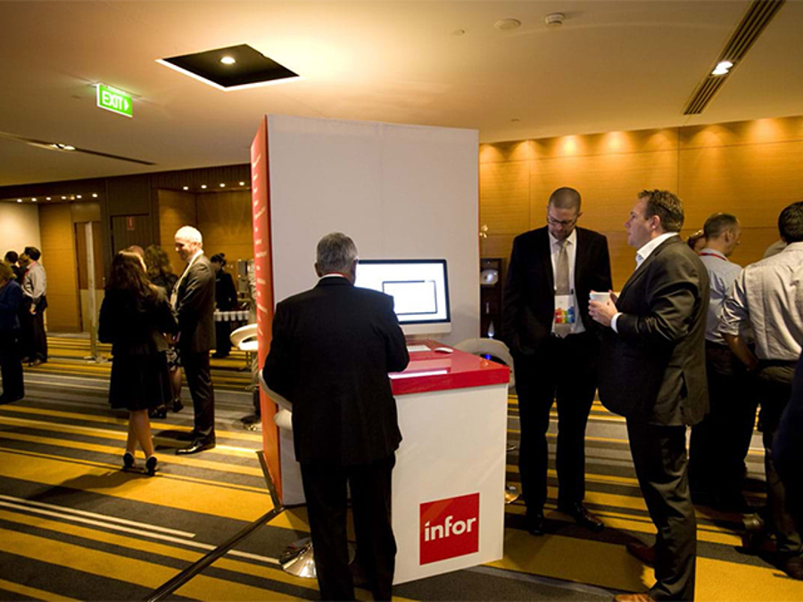 Delegate at a white kiosk counter with a red top and a screen, in a busy conference foyer