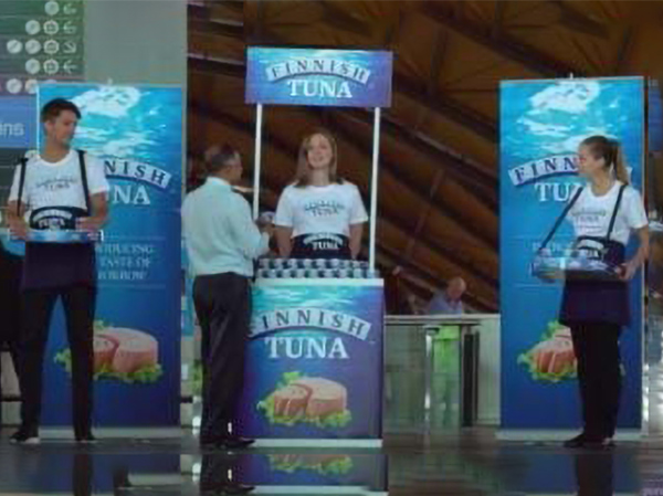 Finnish Tuna sampling in a station concourse: a branded counter with header, two pull-up banners and two staff carrying branded vendor trays