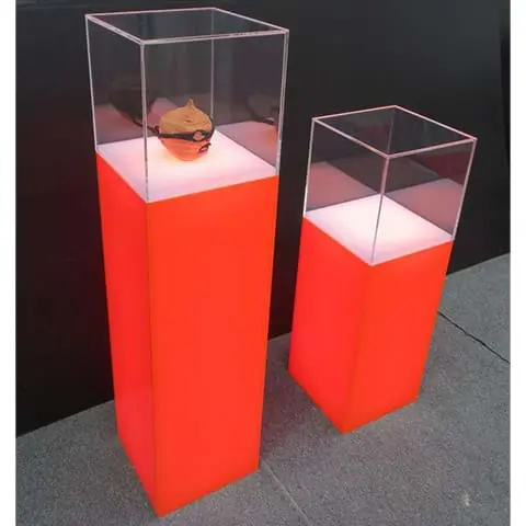 Two orange plinths at different heights with lit white tops under clear perspex cases