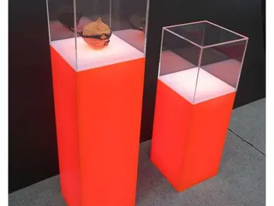 Two orange plinths at different heights with lit white tops under clear perspex cases
