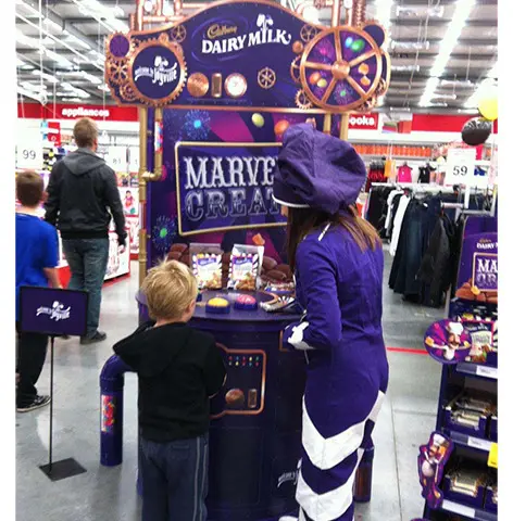 Costumed promoter at a round Cadbury Marvellous Creations counter under a tall cog-style header