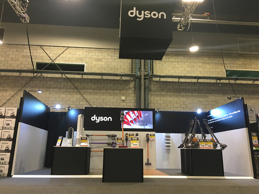 Dyson stand with a hanging branded sign, spotlights on arms along the walls, a screen and vacuum cleaners on black plinths