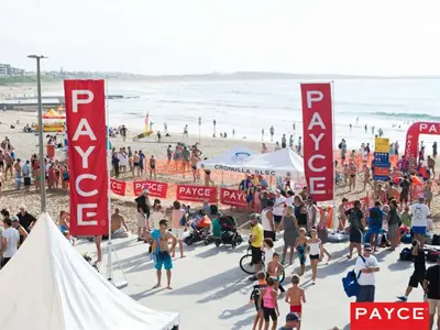 Red PAYCE flags and mesh barrier panels along the sand at a Cronulla surf event