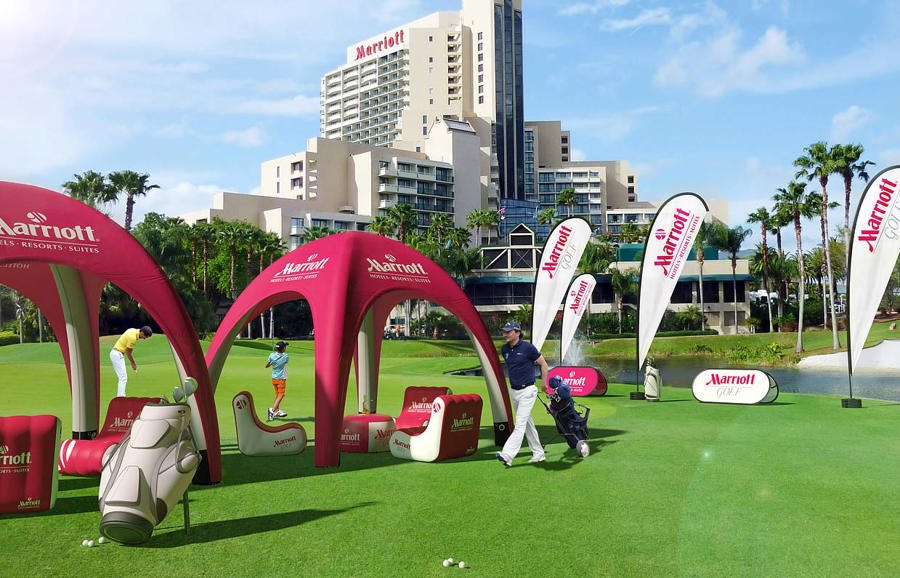 Corporate golf day on a golf course with two branded inflatable gazebos, inflatable armchairs, an inflatable golf bag and teardrop flags