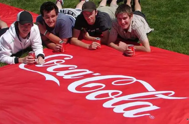 Red Coca-Cola ground mat with a white script logo spread across the grass