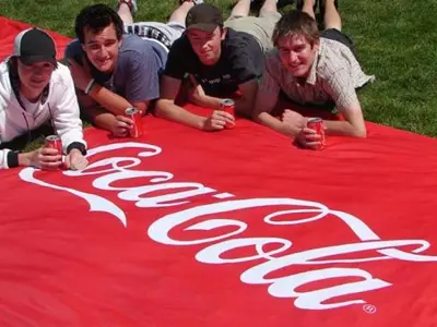 Red Coca-Cola ground mat with a white script logo spread across the grass