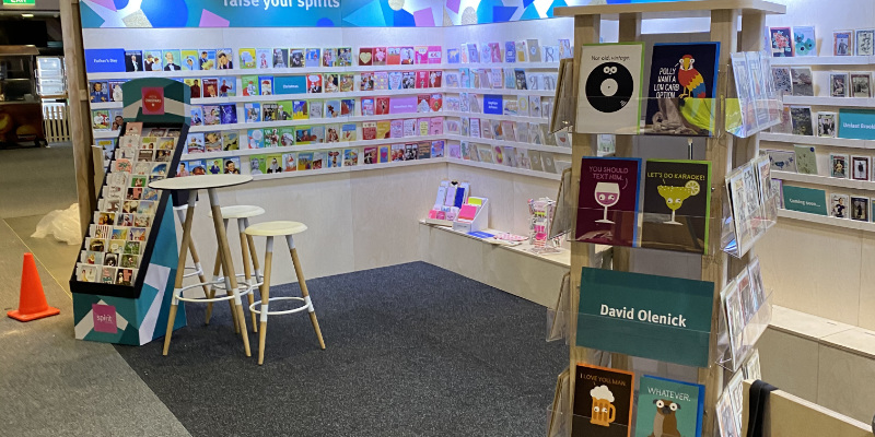 Greeting card exhibition stand with full-height card shelving, timber card display towers and a bar table with stools
