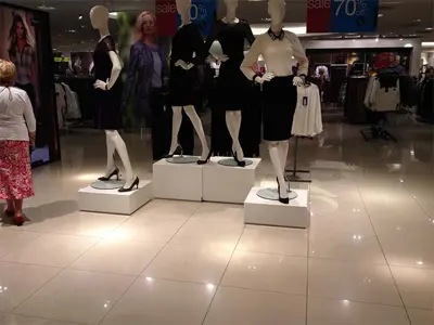 Mannequins on white square blocks at two heights on a department store fashion floor