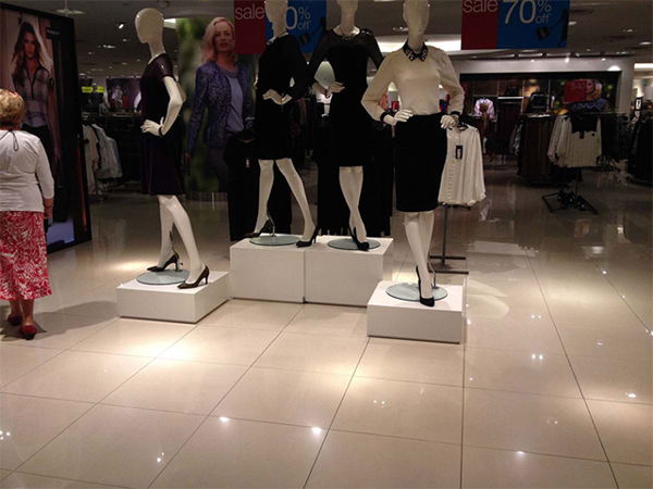 Low white square plinths of different heights in a department store, each carrying a mannequin on a small round base