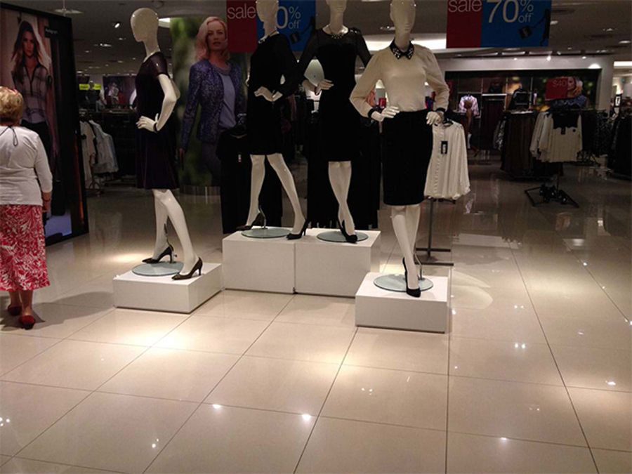 Low white square plinths of different heights in a department store, each carrying a mannequin on a small round base