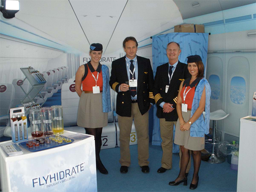 FlyHidrate tasting stand themed as an aircraft cabin, with printed seat rows and windows and staff dressed as pilots and flight attendants