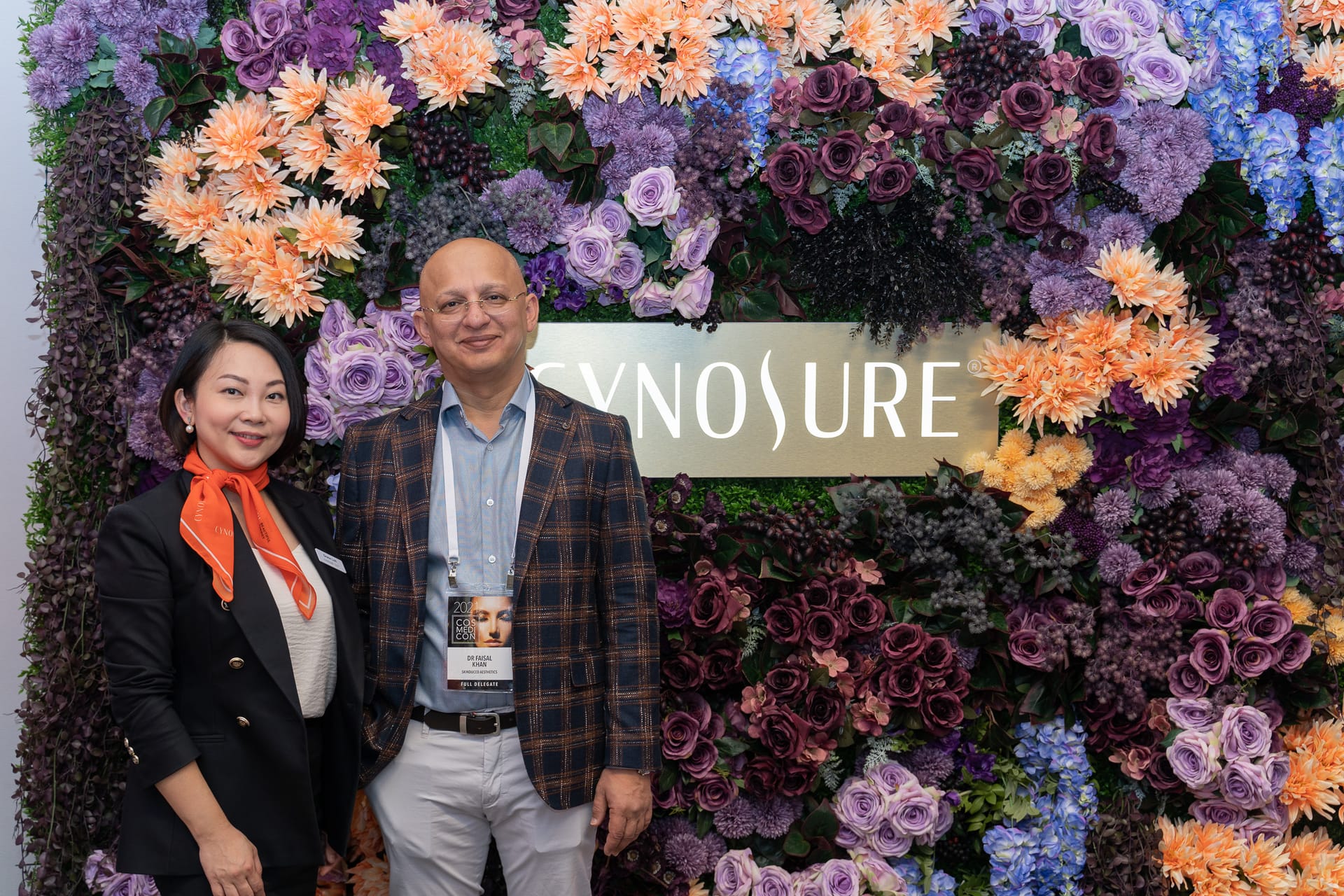 Two Cynosure guests posing in front of a flower wall with a Cynosure sign