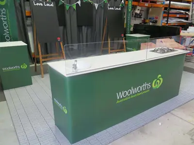 Green Woolworths mobile kitchen with a sink and gas cooktop behind clear screens