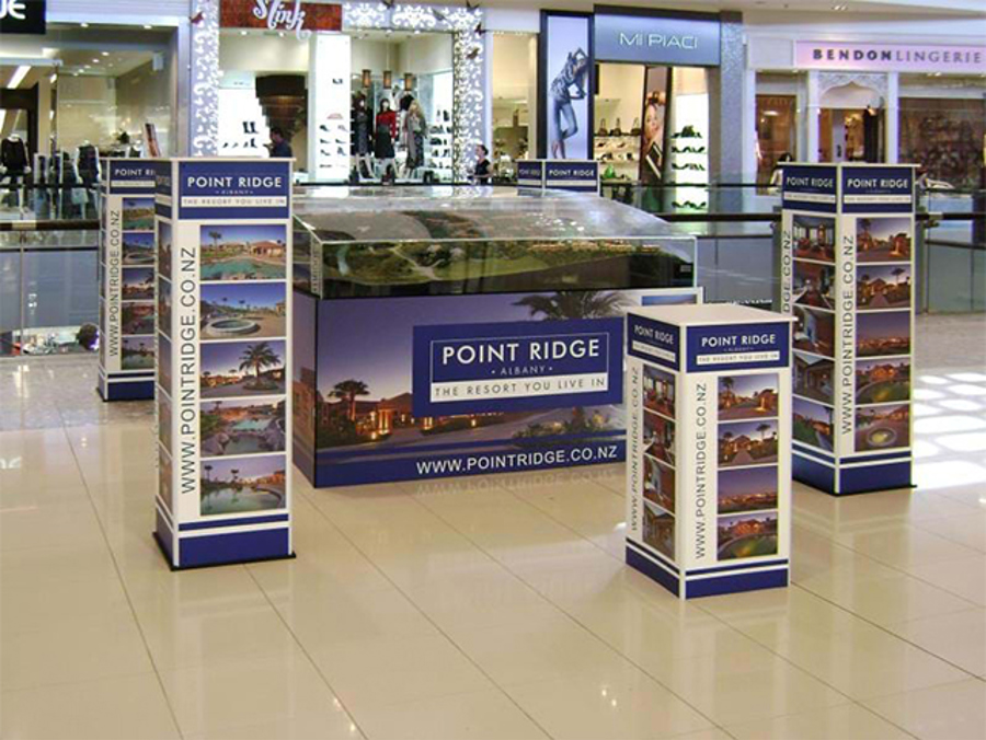Property development display in a shopping centre walkway, with a scale model under a glass case surrounded by four printed display towers