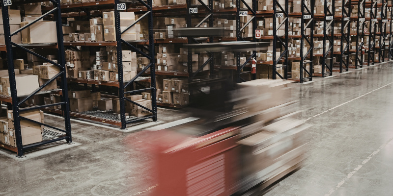 Warehouse aisle with racking full of boxes and a forklift moving past