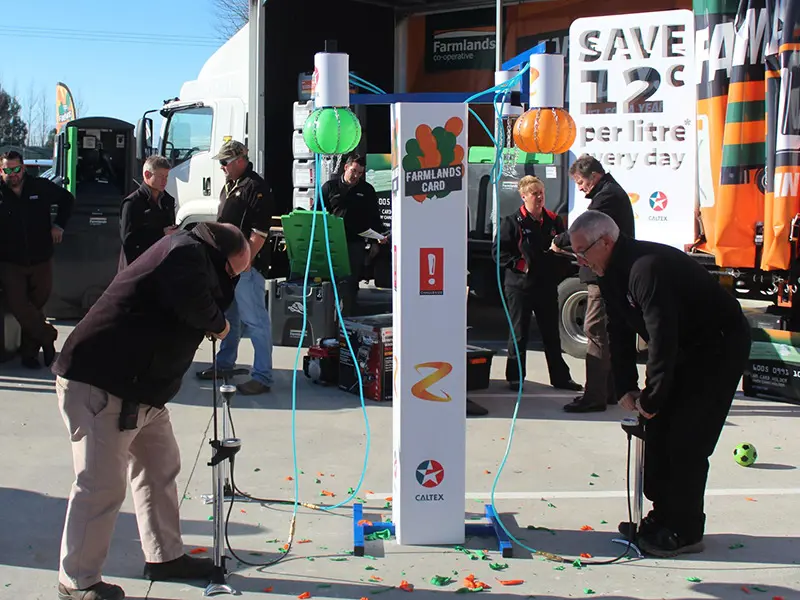 Two players inflating balloons on a Farmlands Card and Caltex tower while a crowd watches