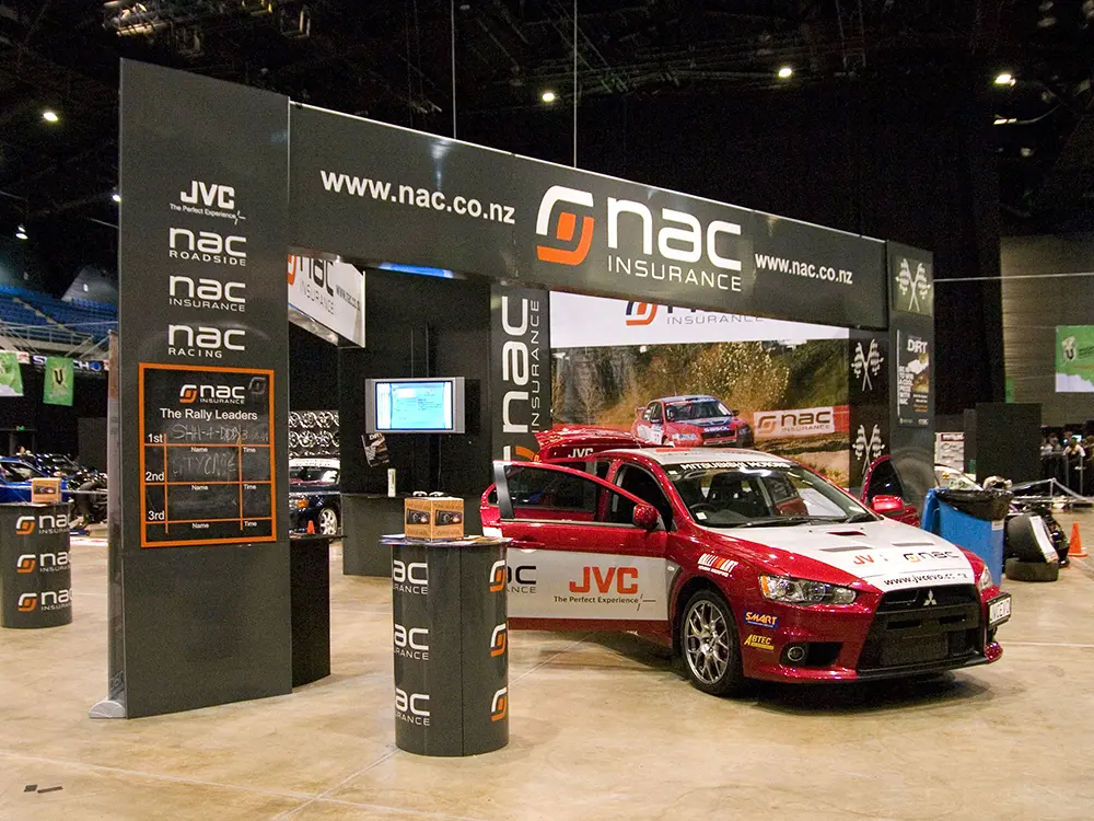 JVC-branded rally car on an NAC Insurance stand with a black fascia and round plinths