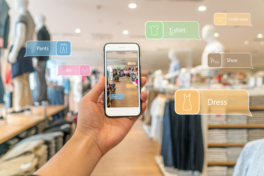 Phone held up in a clothing store, with augmented-reality labels such as T-shirt and Dress floating over the racks