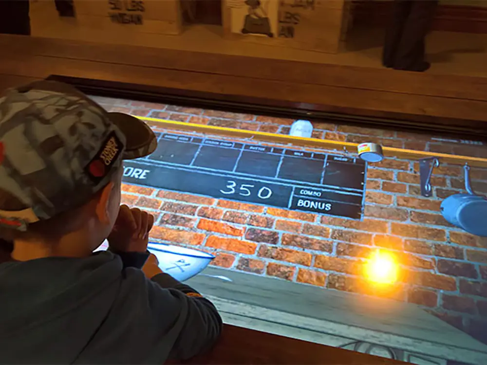 Child playing a custom game on a touch screen framed in timber at an exhibition