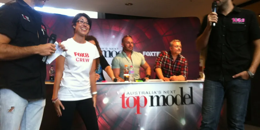 Presenter interviewing contestants in front of the Australia's Next Top Model backdrop