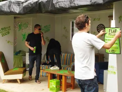 V's Big Flat Free-For-All room set with a sofa, dartboard and green campaign wall graphics