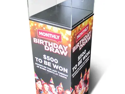 Clear Monthly Birthday Draw box on a plinth wrapped in party imagery and draw details