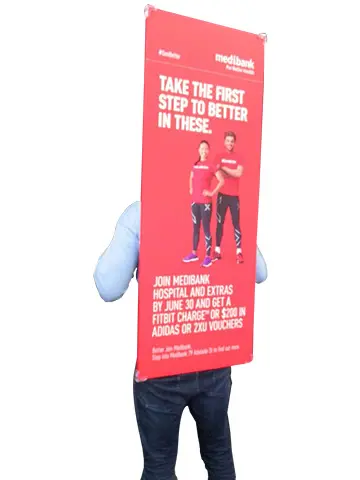Promoter carrying a tall printed Medibank board strapped over the shoulders, rising above head height