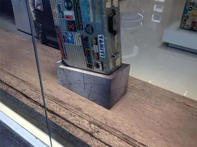 Stone-look plinth raising a sticker-covered aluminium suitcase in a shop window