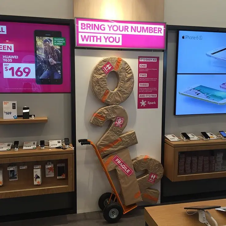 Spark in-store display with oversized parcel-wrapped numbers on a hand trolley under a pink lightbox