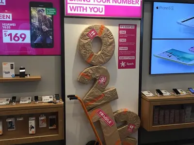 Spark in-store display with oversized parcel-wrapped numbers on a hand trolley under a pink lightbox