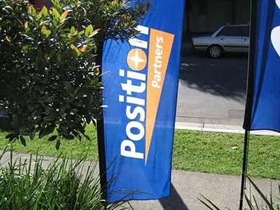 Blue Position Partners bow flag with an orange accent beside a footpath and garden