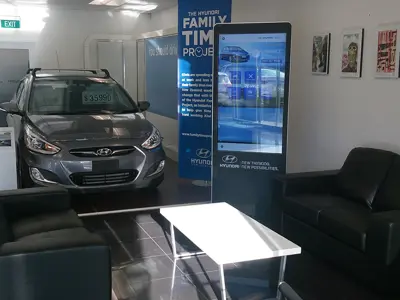 Hyundai portrait screen kiosk in black housing between a display car and showroom sofas