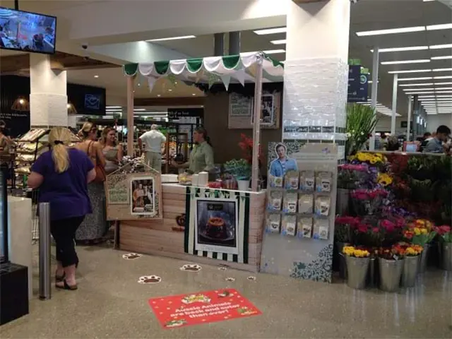 Woolworths Christmas recipe kiosk with green and white scalloped trim beside a flower stand