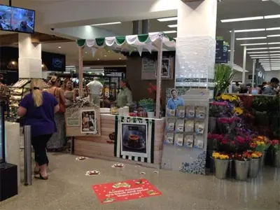 Woolworths Christmas recipe kiosk with green and white scalloped trim beside a flower stand