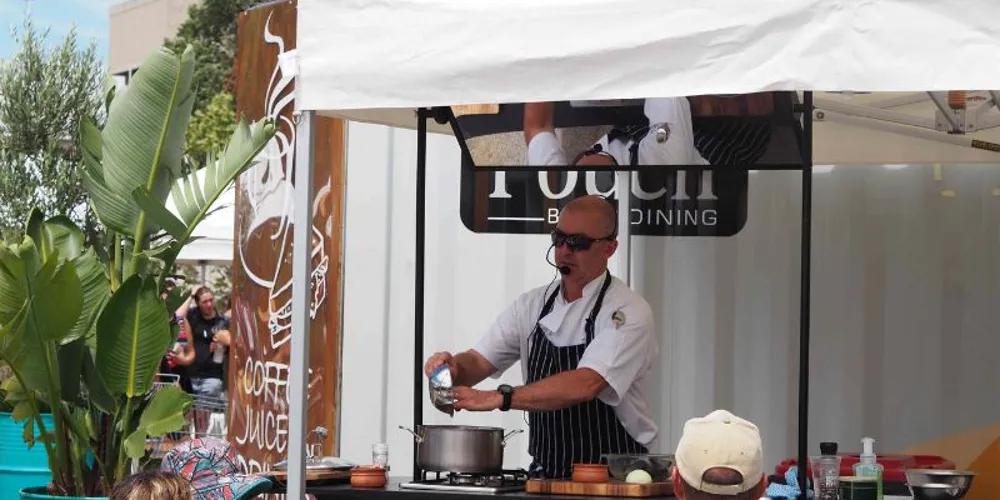 Chef cooking at the demonstration bench under a marquee at Dandenong Market