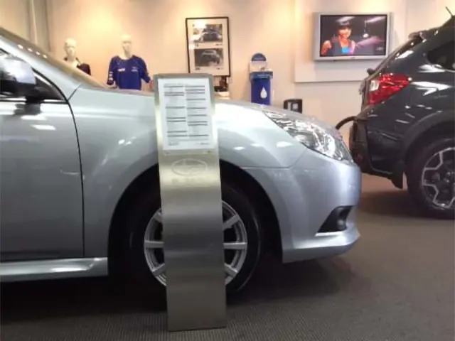 Curved brushed-metal stand holding a specification sheet beside a silver Subaru in a showroom