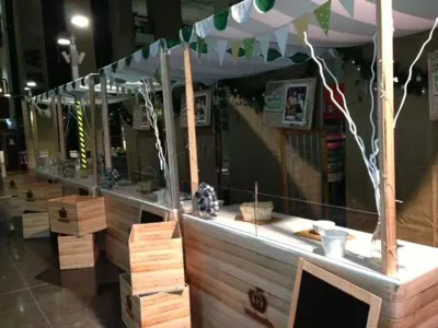 Row of Woolworths market stalls with fabric roofs, green bunting and clear serving screens