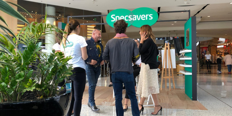 Specsavers Westfield pop-up stand with an overhead logo sign, green frame display tower and planters