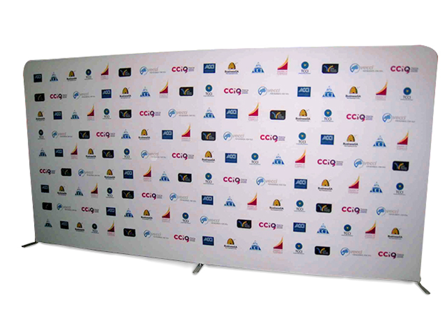 Wide free-standing fabric media wall with rounded corners on low feet, printed with rows of small repeating sponsor logos on a white background
