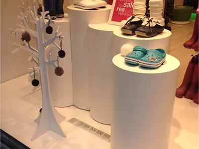 White cylinders at staggered heights holding winter boots, clogs and children's shoes